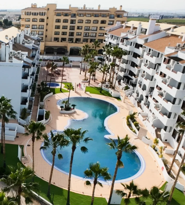 Uitzicht van boven op een modern appartementencomplex in Los Alcázares met groot zwembad, palmbomen en witte gebouwen rondom de binnentuin